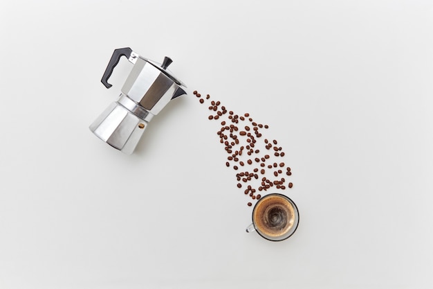 Grains de café sous la forme d'une goutte dégoulinant d'une cafetière en métal dans une tasse sur fond blanc