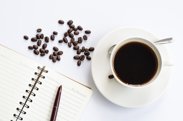 Grains de café et tasse de café sur blanc avec carnet et stylo