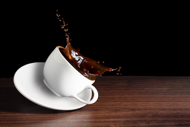 Grains de café, tasse de café avec un effet d'éclaboussure sur un bureau marron