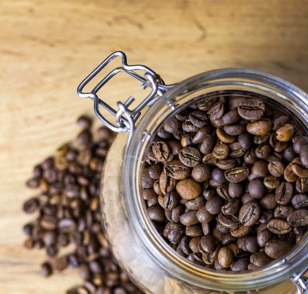 Grains de café torréfiés en boîte de verre sur table en bois