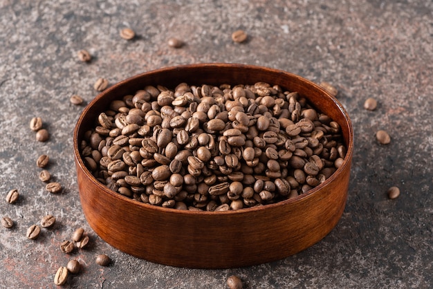 Grains de café torréfiés dans une boîte en bois sur fond sombre.