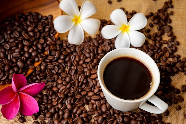 Grains de café torréfiés dans un bol en bois à côté de la tasse de café