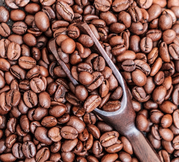 Grains de café torréfiés dans une cuillère en bois sur fond noir