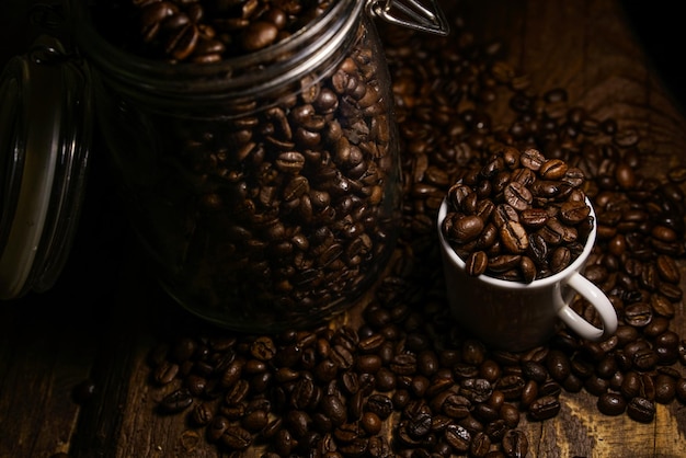 Des grains de café torréfiés dans un pot en verre et une tasse sur la table