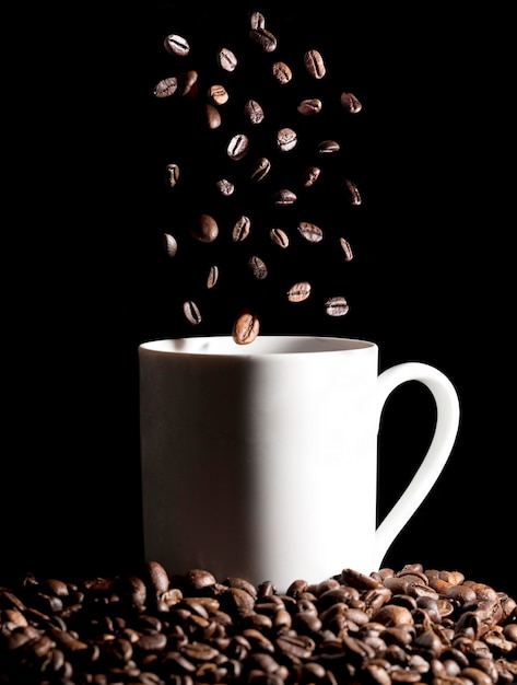 Grains de café torréfiés dans une tasse de café, isolés sur fond noir
