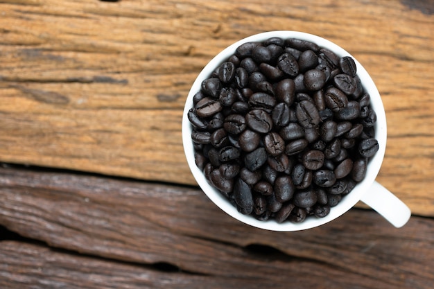 Grains de café torréfiés dans un verre blanc sur fond en bois