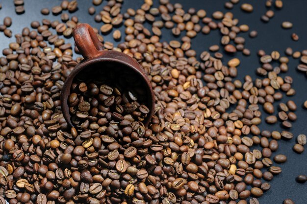 Grains de café torréfiés dispersés et une tasse sur un fond sombre