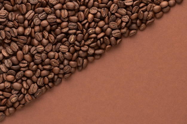 Grains de café torréfiés sur fond marron avec copie espace vue de dessus en gros plan