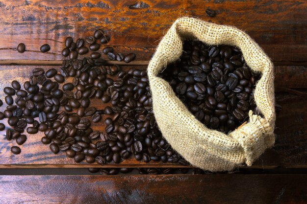 Grains de café torréfiés et frais dans un sac en tissu rustique et versés sur une table en bois rustique. Vue de dessus