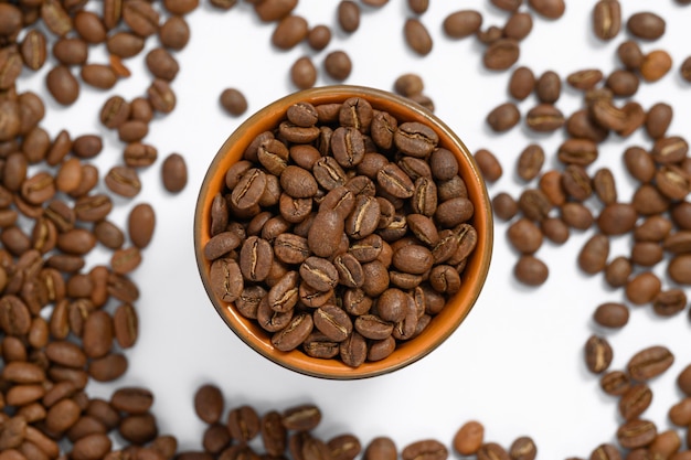 Grains de café torréfiés parfumés sur fond blanc et une petite tasse