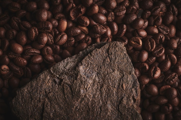 Grains de café torréfiés sur socle en pierre fond brun