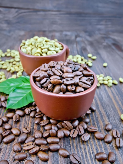 Photo grains de café vert et noir dans des tasses d'argile brune et sur une table avec des feuilles sur un fond de planche de bois