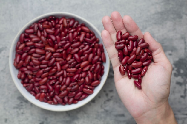 Grains de haricot rouge à portée de main et dans un bol mis sur fond de béton