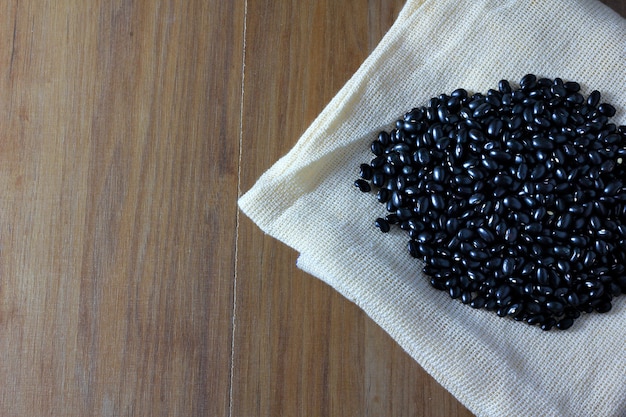 Grains de haricots noirs sur le sac sur le côté de la table en bois, vue de dessus