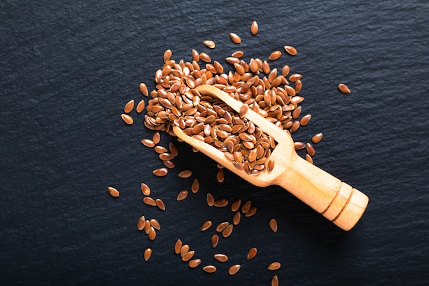 Grains de lin bio dans une cuillère en bois sur un plateau en ardoise noire avec espace de copie