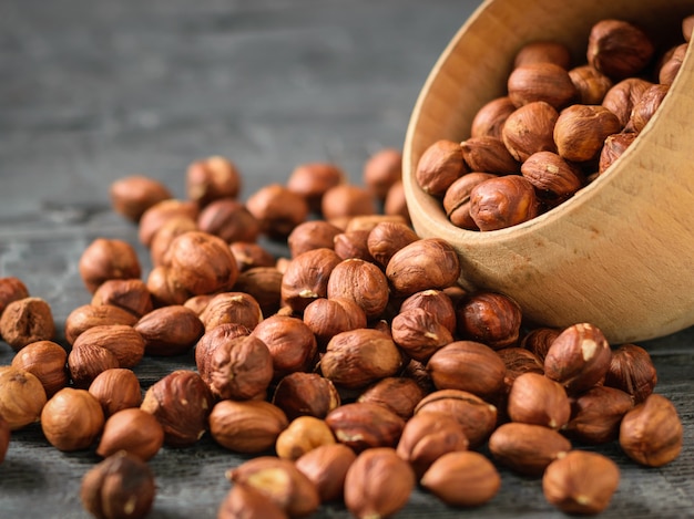 Les grains de noisette sont versés dans un bol en bois sur une table sombre.