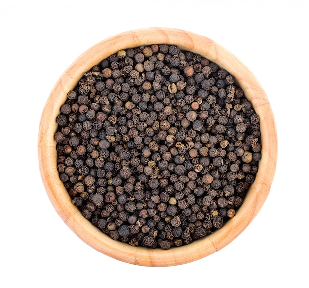 Grains de poivre dans un bol en bois sur mur blanc