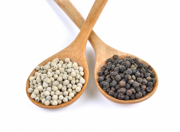 Grains de poivre dans la cuillère en bois sur mur blanc