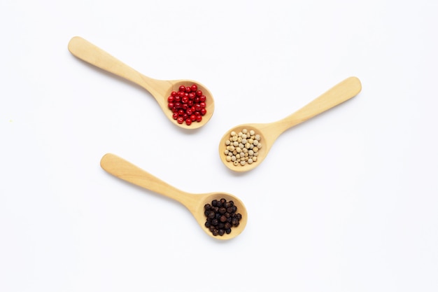 Grains de poivre rouge, blanc et noir avec une cuillère en bois blanche.