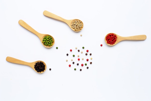 Grains de poivre rouge, vert, blanc et noir avec une cuillère en bois blanche.