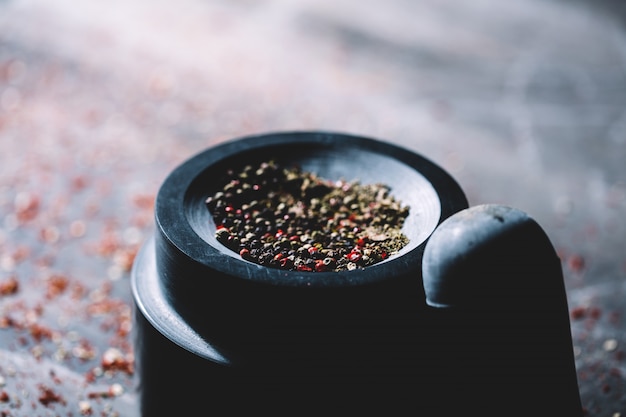 Grains de poivre séché demi-broyés placés dans un mortier.