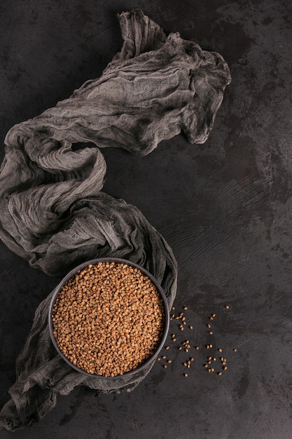 Grains de sarrasin dispersés non cuits biologiques dans un bol sur table noire. Concept d'aliments sains et diététiques. Vue de dessus.