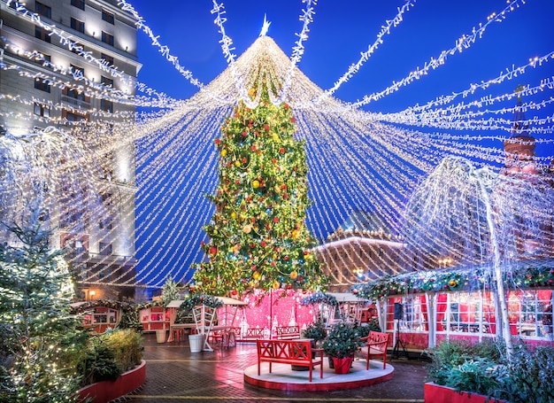 Grand arbre de Noël sur la place Manezhnaya à Moscou, bancs et maisons à la lumière des veilleuses festives