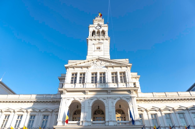 Un grand bâtiment blanc avec une horloge sur le devant et un ciel bleu derrière.