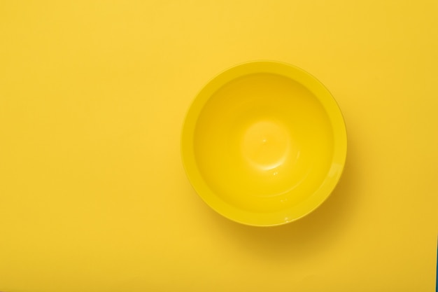 Un grand bol jaune foncé sur fond jaune. Ustensiles en plastique pour la cuisine.