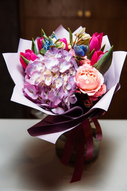 Un grand bouquet de fleurs colorées de différentes sortes se trouve dans un vase en verre transparent.