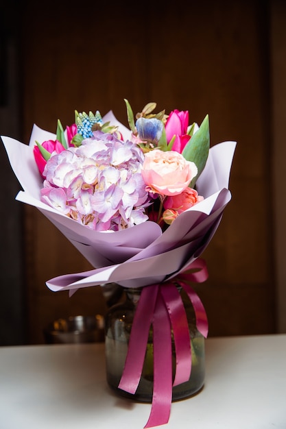 Un grand bouquet de fleurs colorées de différentes sortes se trouve dans un vase en verre transparent.