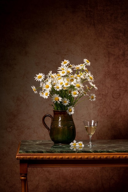 Un grand bouquet de marguerites dans un vase marron sur une table en marbre vert à côté des côtés de vin blanc