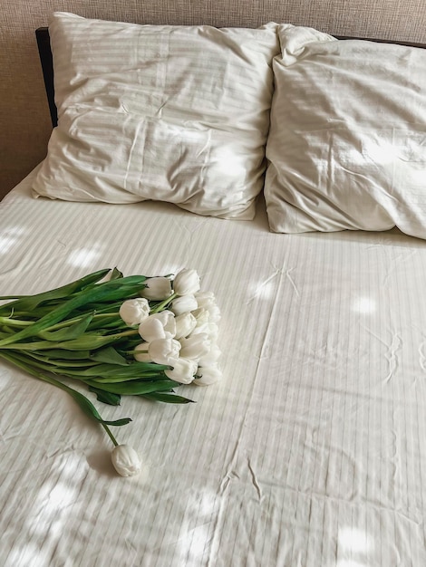 Photo un grand bouquet de tulipes blanches est allongé sur le lit sur le linge de lit blanc surprise d'anniversaire jour de la saint-valentin jour international de la femme