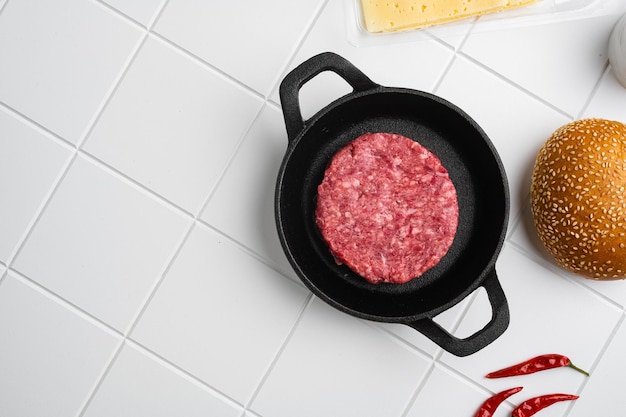 Grand burger de boeuf frais cru sur fond de table en carreaux de céramique blanche vue de dessus à plat avec espace de copie pour le texte