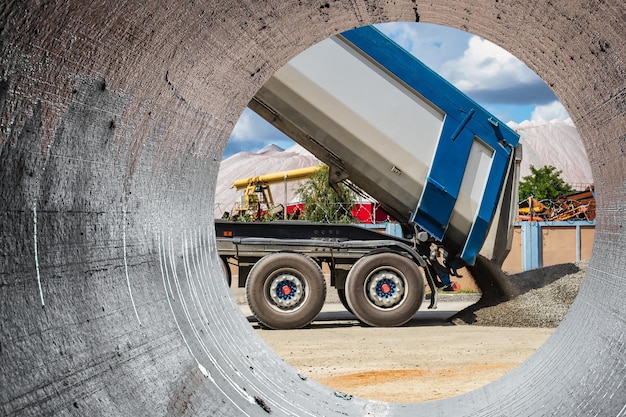 Un grand camion à benne basculante décharge des gravats ou du gravier sur un chantier de construction Tonar de voiture pour le transport de marchandises en vrac lourdes Fourniture de matériaux au chantier de construction Vue depuis un grand tuyau en béton