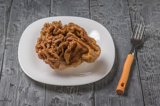 Un grand champignon gyromitra sur une plaque blanche avec une fourchette sur une table en bois Champignons de printemps