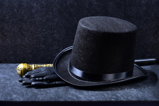 Un grand chapeau de magicien, des gants en cuir et une canne à pommeau sur fond noir