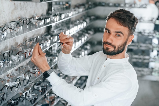 Grand choix Homme élégant avec barbe choisissant des lunettes dans le magasin d'optique