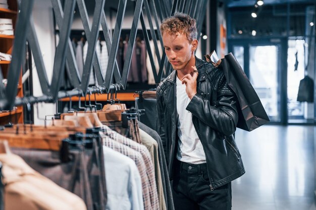 Grand choix Jeune homme dans un magasin moderne avec de nouveaux vêtements Vêtements élégants et chers pour hommes