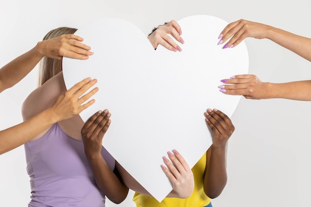 Photo un grand cœur blanc porté par huit mains de différentes nations et races.