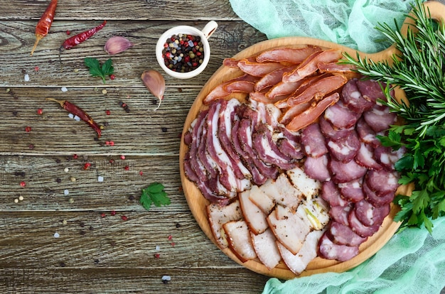 Grand ensemble de viande. Saucisse de porc-boeuf fumé maison, bacon salé, tranches de basturma hachées sur une planche de bois avec des épices et des herbes. Mise à plat. La vue de dessus