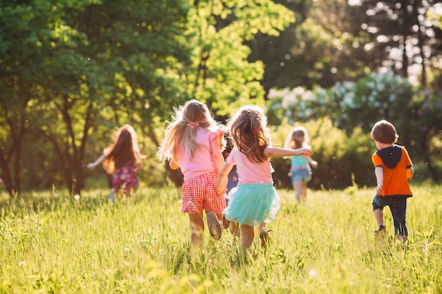 Grand groupe d&#39;enfants, d&#39;amis garçons et filles courir dans le parc sur une journée d&#39;été ensoleillée en vêtements décontractés.