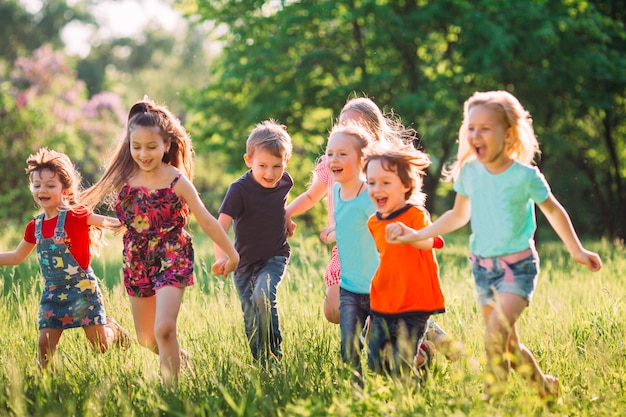 Grand groupe d&#39;enfants, d&#39;amis garçons et filles courir dans le parc sur une journée d&#39;été ensoleillée en vêtements décontractés.