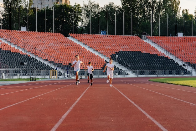 Un grand groupe d'enfants de garçons est enseigné par un entraîneur au départ avant de courir au stade au coucher du soleil Un mode de vie sain