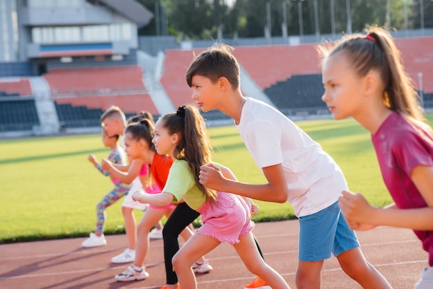 Un grand groupe d'enfants, garçons et filles, courent et font du sport au stade pendant le coucher du soleil. Un mode de vie sain.