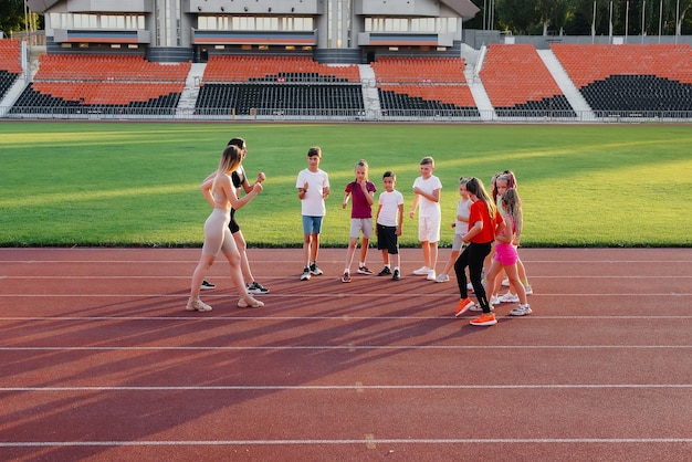 Un grand groupe d'enfants garçons et filles s'échauffent et s'entraînent sous la direction d'un entraîneur au stade au coucher du soleil Un mode de vie sain