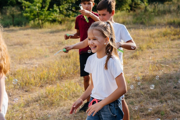 Un grand groupe d'enfants joyeux jouent dans le parc et gonflent des bulles de savon. Jeux dans un camp pour enfants.