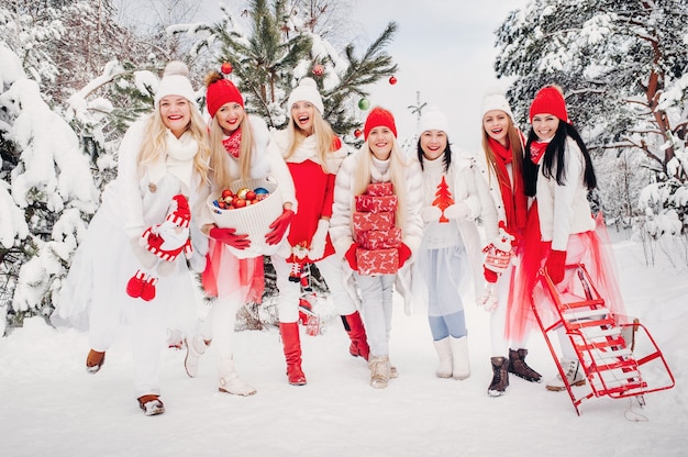 Un grand groupe de filles avec des cadeaux de Noël dans leurs mains debout dans la forêt d'hiver. Filles en vêtements rouges et blancs avec des cadeaux de Noël dans la forêt enneigée