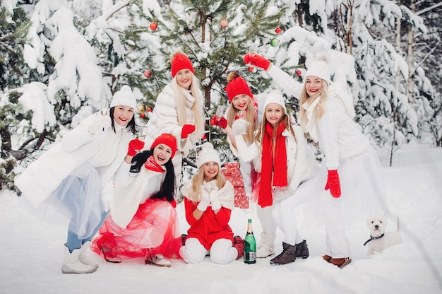 Un grand groupe de filles avec des coupes de champagne à la main se tient dans la forêt d'hiver. Des filles en vêtements rouges et blancs avec des boissons du nouvel an dans une forêt enneigée.