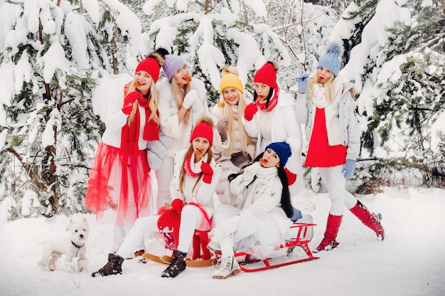 Un grand groupe de filles avec des sucettes à la main se tient dans la forêt d'hiver. Des filles en vêtements rouges et blancs avec des bonbons dans une forêt enneigée.